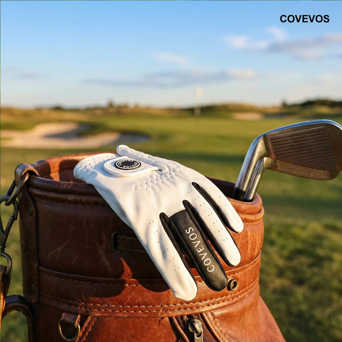 Gant blanc avec le logo Covevos reposant sur le dessus d'un sac de golf en cuir marron.