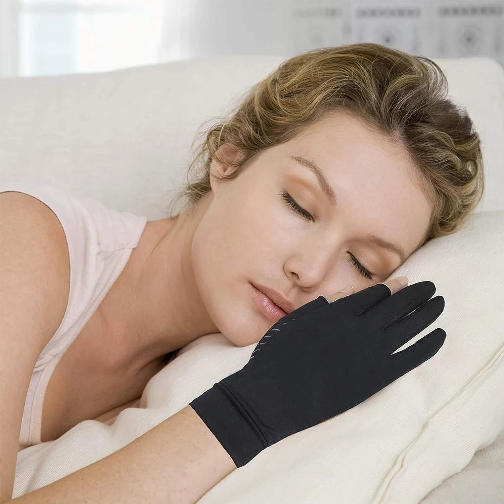 A woman is wearing black copper arthritis relief gloves while resting on a white pillow.