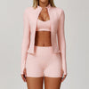 A woman models a pink 3-piece yoga sports set consisting of a long-sleeved jacket, cropped top, and shorts.