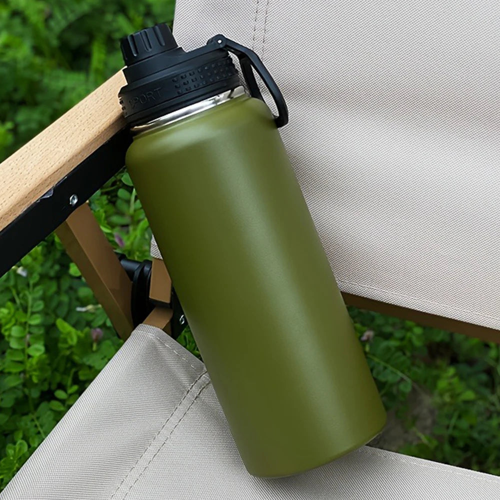 A matte olive green insulated stainless steel vacuum water bottle resting on a light-colored outdoor fabric surface.