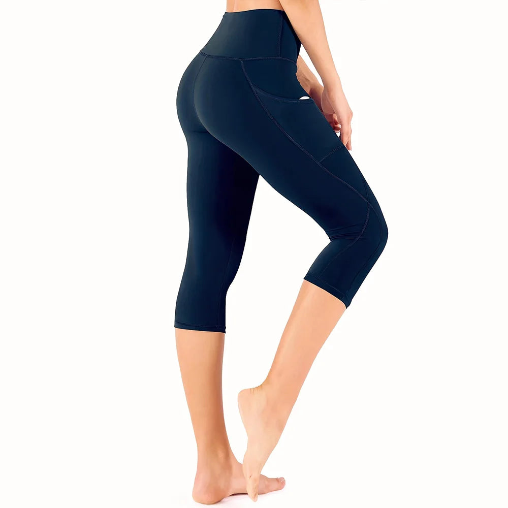Una persona vistiendo leggings capri de yoga de cintura alta y color azul oscuro con bolsillos de costura.