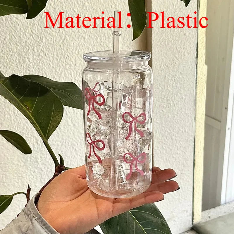 Clear plastic tumbler water bottle with pink bow decorations and a straw being held by a hand.