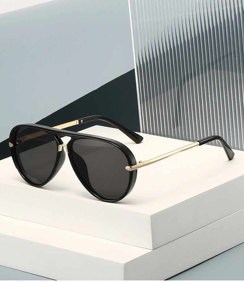 A pair of black retro pilot sunglasses with gold accents resting on a white surface.