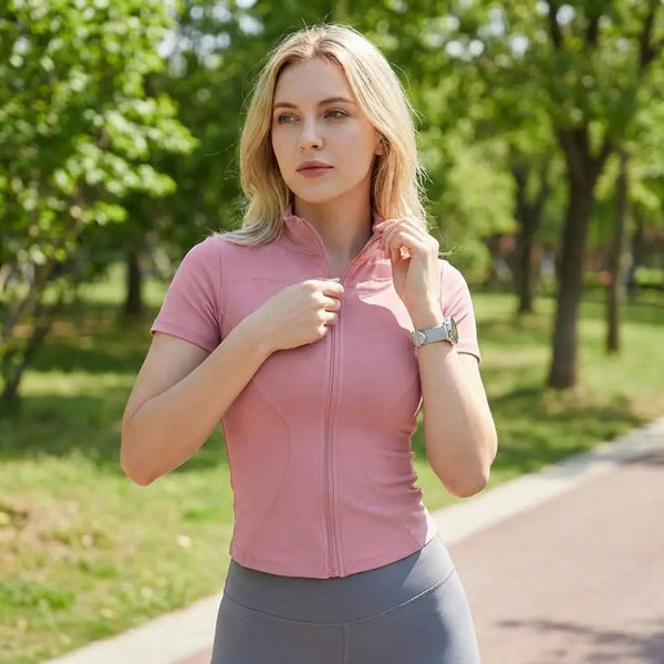 A woman wearing a pink lightweight slim fit sports yoga top is walking outdoors in a park.