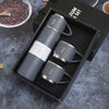 A black box contains a set of four grey stainless steel vacuum flasks and a fifth flask, resting on a dark surface.