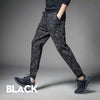A man wearing black camouflage elastic waist drawstring pants and a dark top, shown from the side.