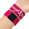 A magenta wristband bracelet with white text and a black square accent is worn on a person's arm.