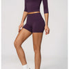 A woman models a purple yoga and fitness leggings set, featuring long-sleeved top and short bottoms.