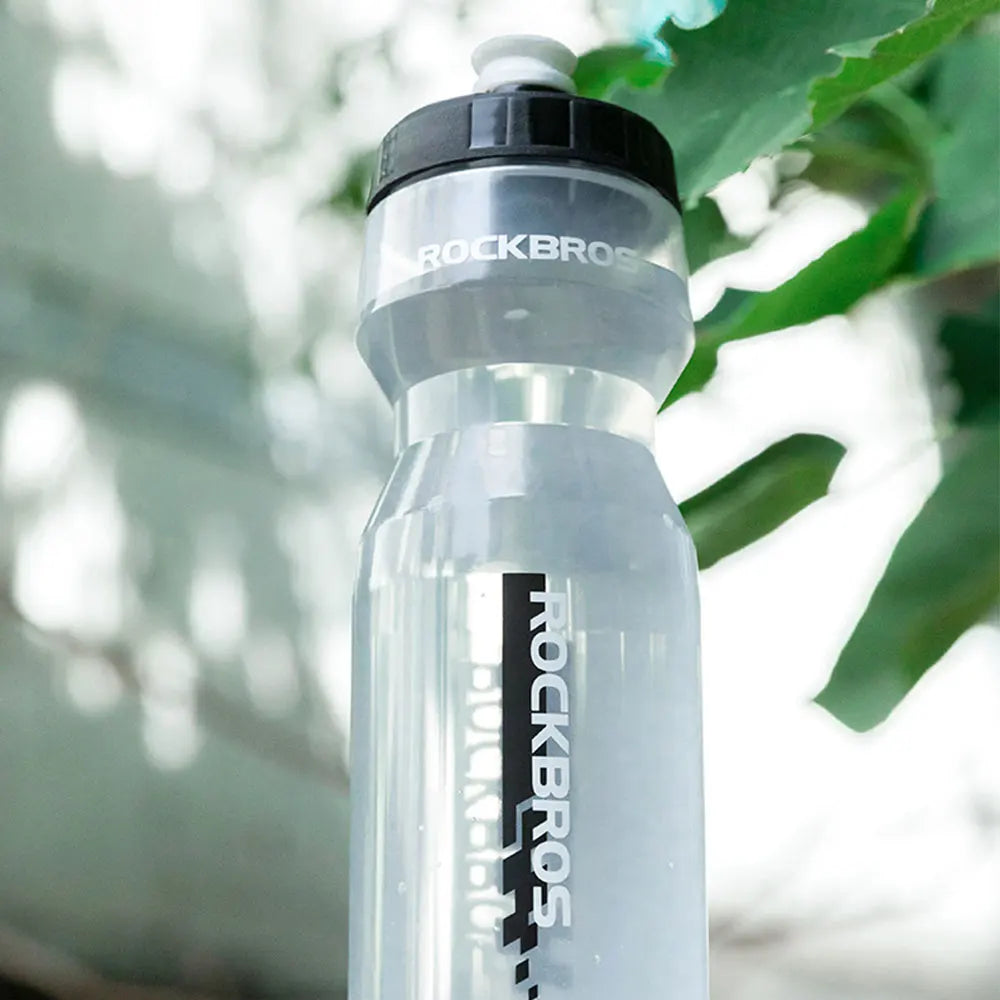 A clear plastic sports water bottle with a black cap and the ROCKBROS logo visible, set against a blurred green background.