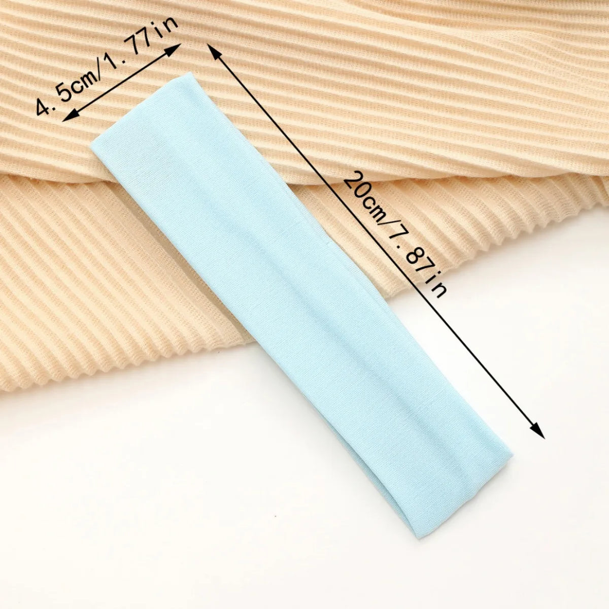 Light blue stretchable cotton sweat absorbing headband shown next to a beige ribbed fabric with dimension markings.