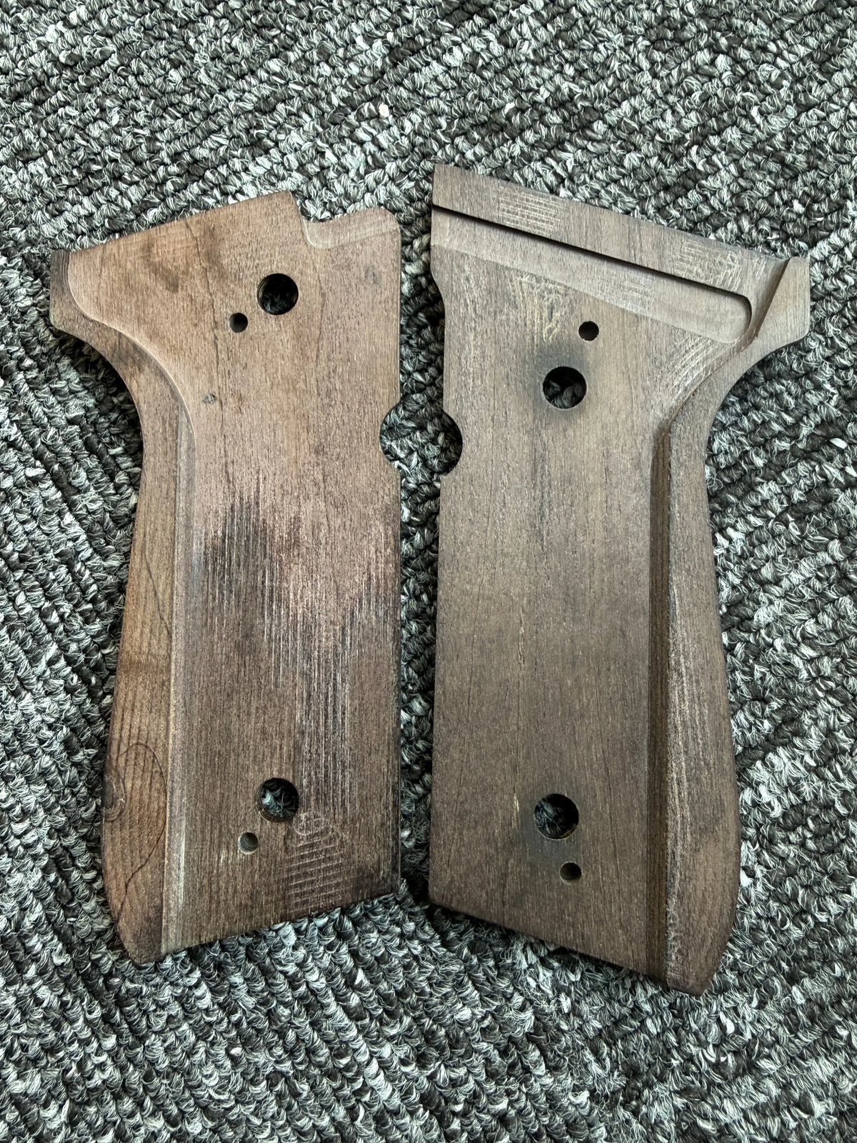 Two wooden custom diamond pattern grips for a firearm resting on a gray textured surface.