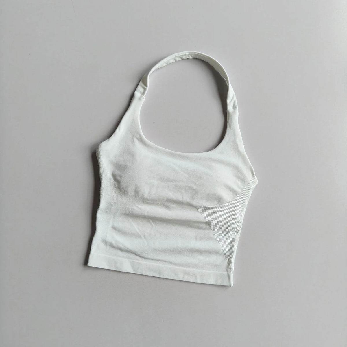 A white seamless yoga and pilates sports bra laid flat on a light gray surface.