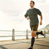 A man running outdoors in a gray t-shirt and shorts near the water.