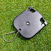 A black portable golf score counter with a metal chain attached, resting on green grass.