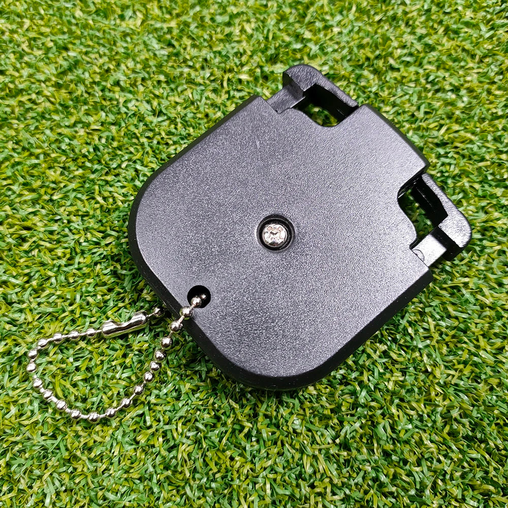 A black portable golf score counter with a metal chain attached, resting on green grass.