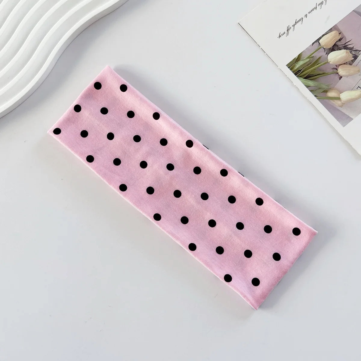 Un bandeau de yoga élastique à pois roses posé sur une surface blanche.