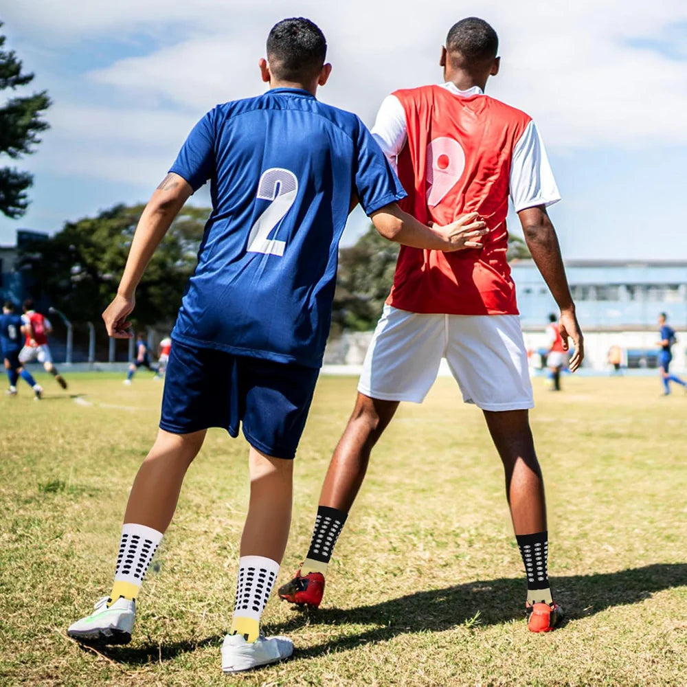Zwei männliche Fußballspieler tragen Griffsocken und Sportkleidung und üben auf einem Rasenfeld.