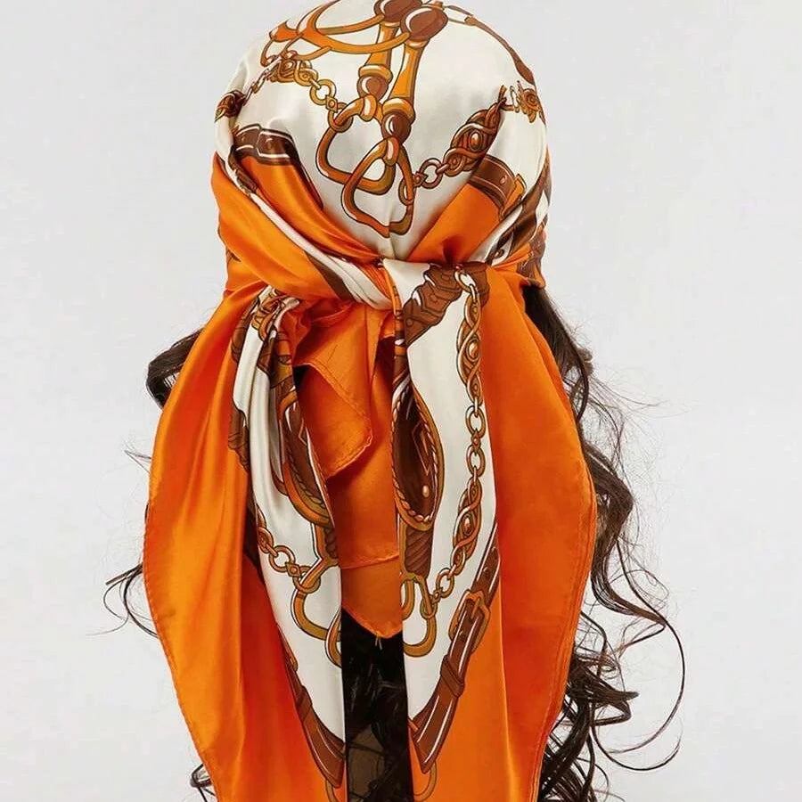 An orange satin square scarf with gold chain detailing tied around a person's hair.