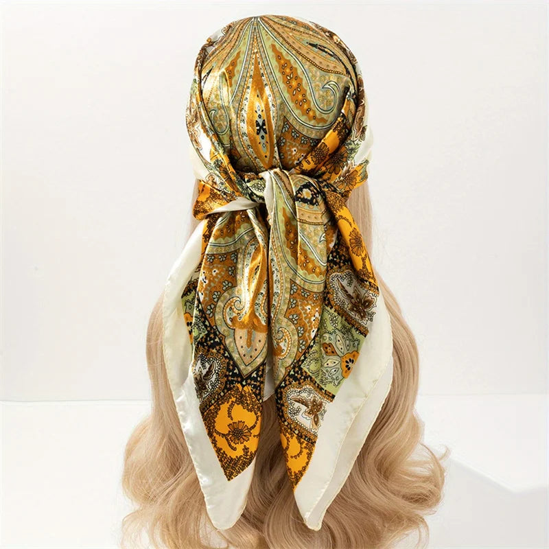 An elegant satin square scarf featuring an ornate gold and olive pattern tied around a blonde hairstyle.