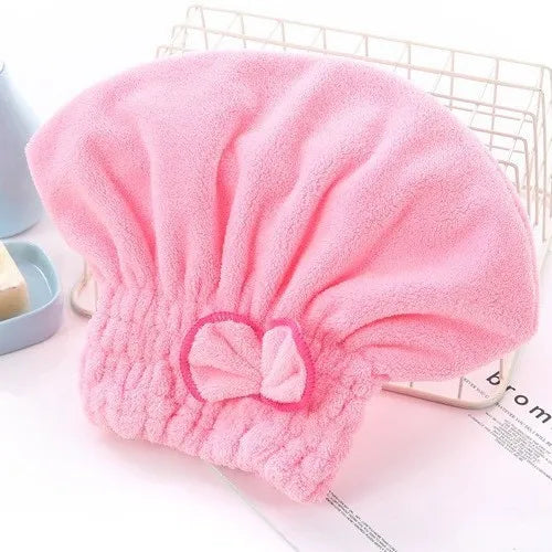 A pink, fluffy hair drying towel cap with a bow detail is shown on a white surface.