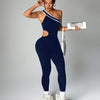 A woman wearing a navy blue seamless yoga jumpsuit with a cutout and white sneakers.