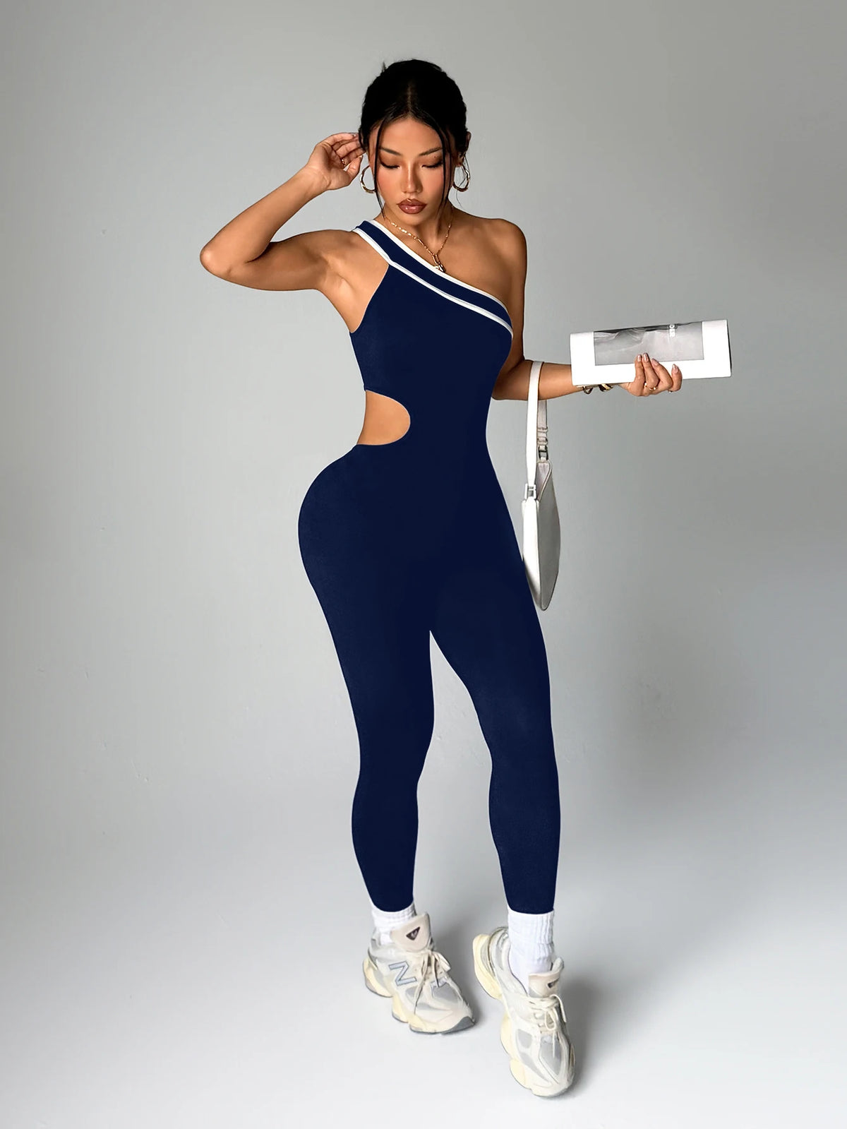 A woman wearing a navy blue seamless yoga jumpsuit with a cutout detail and white sneakers.