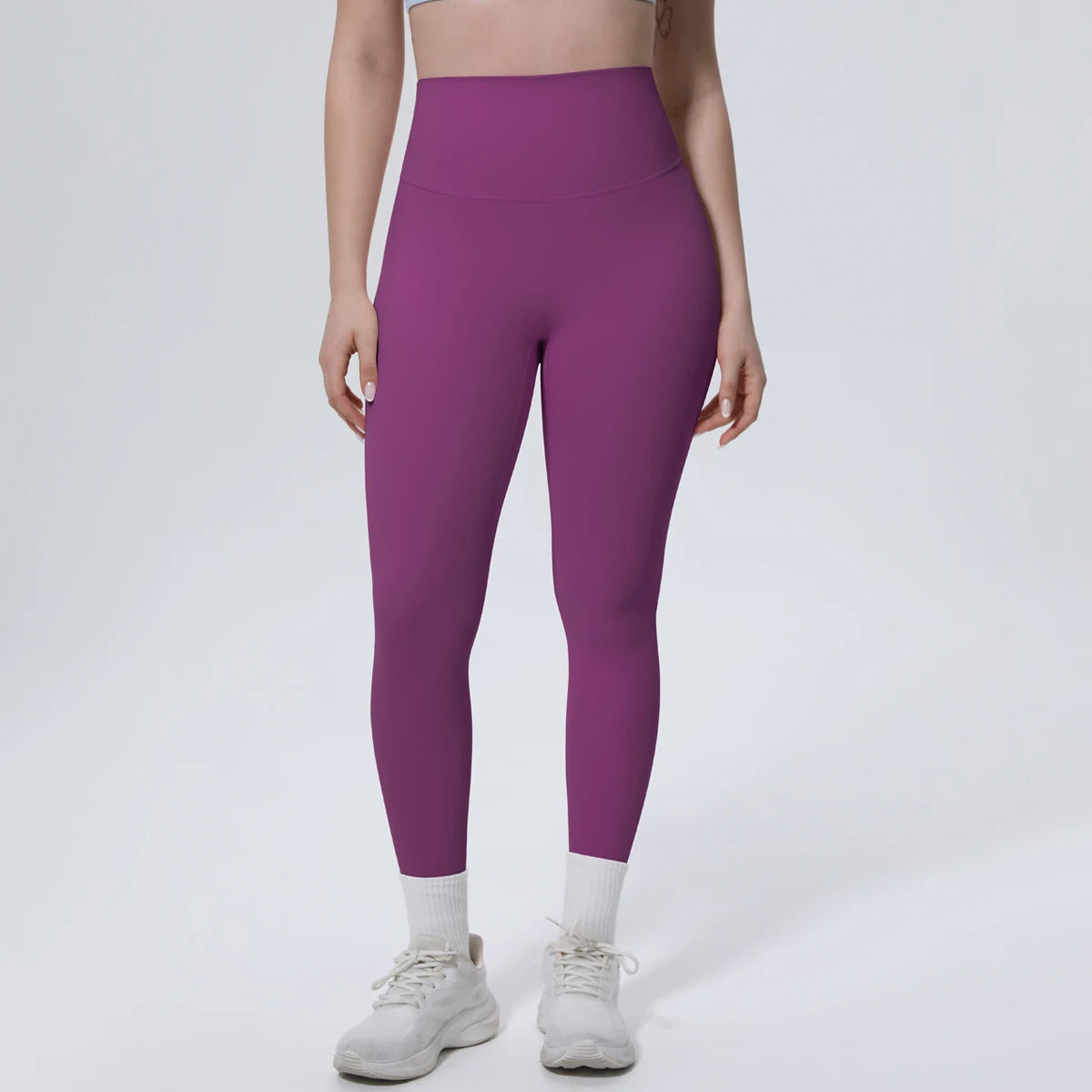 A model wearing high-waisted purple quick-drying yoga and fitness leggings with white socks and white athletic shoes.