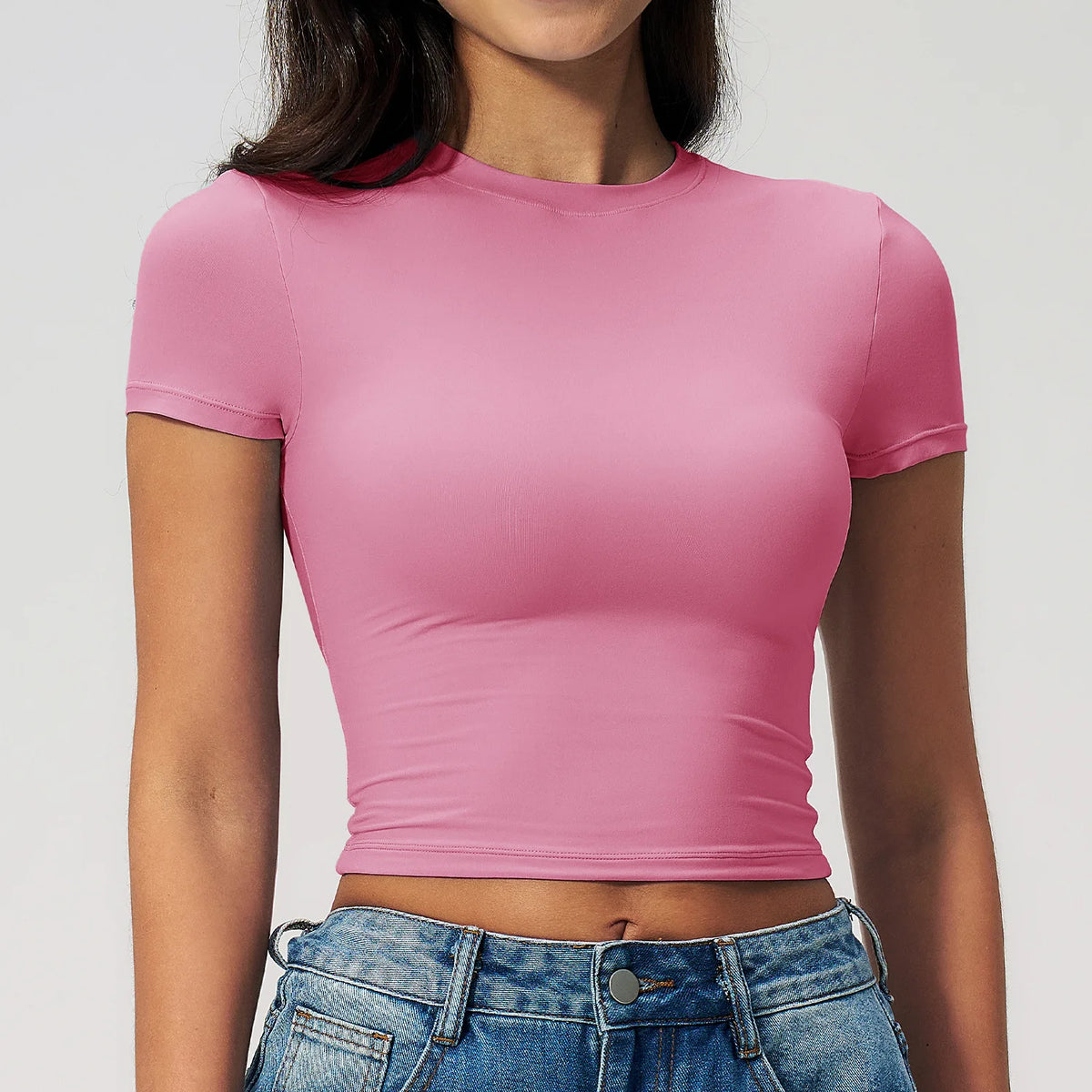 Una modelo vistiendo una camiseta deportiva de yoga y fitness rosa y jeans de mezclilla.