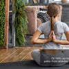 A person is applying therapeutic kinesiology tape to their back while sitting on a yoga mat in a modern interior.