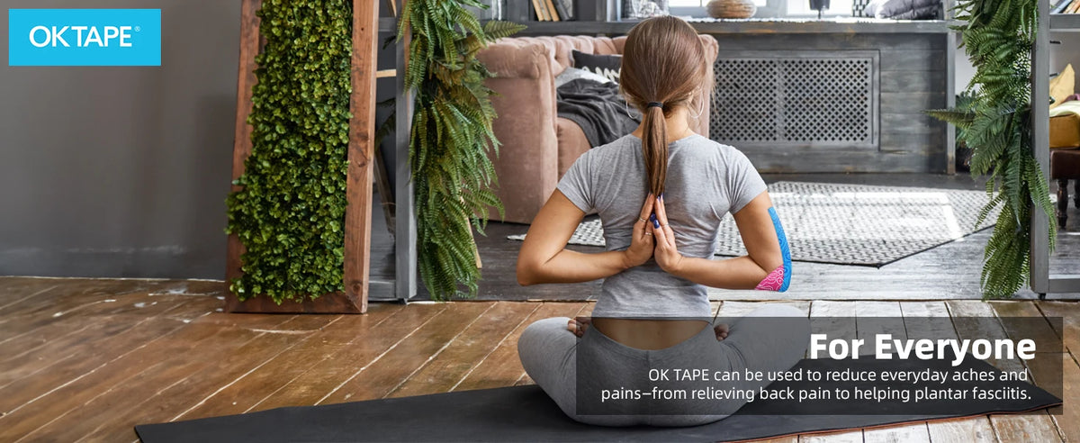 A person is applying therapeutic kinesiology tape to their back while sitting on a yoga mat in a modern interior.