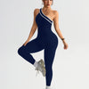 A woman wearing a navy blue seamless yoga jumpsuit with white trim and gray athletic shoes.
