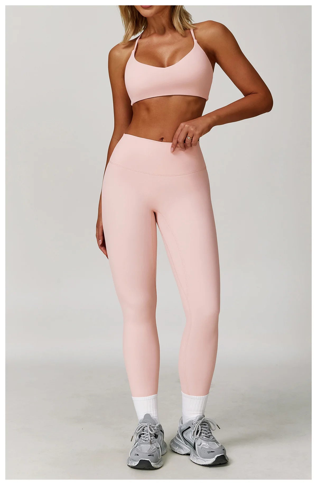 A woman models a pink 3-piece yoga sports set consisting of a cropped top, leggings, and a sports bra.