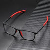 A pair of black vintage square reading glasses with red accents resting on a dark, textured surface.