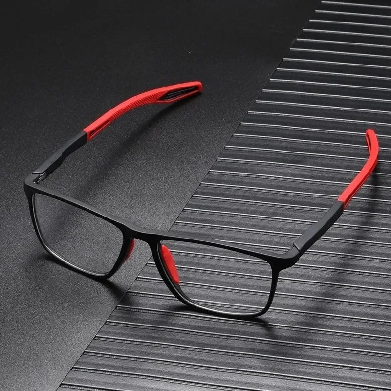 A pair of black vintage square reading glasses with red accents resting on a dark, textured surface.