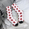 Pair of white mid-calf socks with a repeating pattern of red lip prints on a gray fabric background.