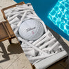 A white Titleist golf ball is resting among numerous white microfiber beach towels on a wooden surface next to blue water.