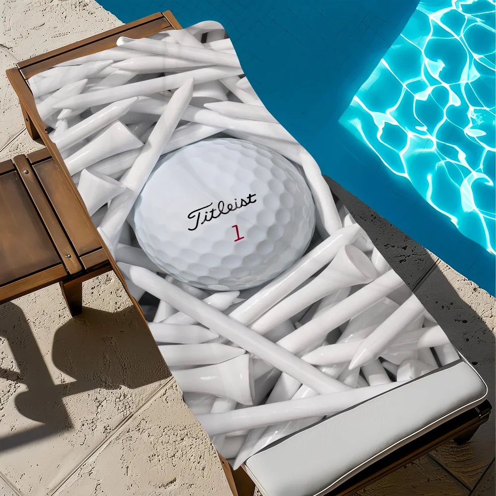 A white Titleist golf ball is resting among numerous white microfiber beach towels on a wooden surface next to blue water.