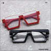 A pair of red and pink oversized square semi-rim metal eyeglasses are displayed on a gray surface.