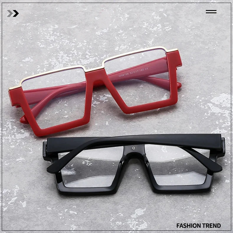A pair of red and pink oversized square semi-rim metal eyeglasses are displayed on a gray surface.