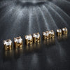 A row of gold-toned magnetic cubic zirconia stud earrings displayed on a dark, textured surface.