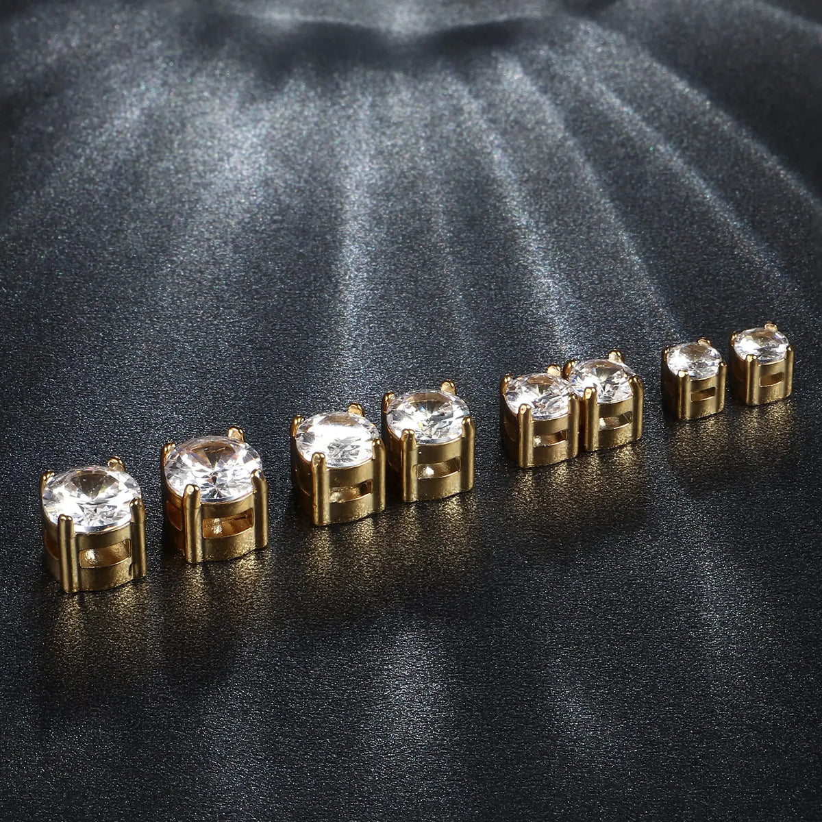 A row of gold-toned magnetic cubic zirconia stud earrings displayed on a dark, textured surface.