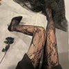 Black floral rattan fishnet hosiery worn on legs and feet.