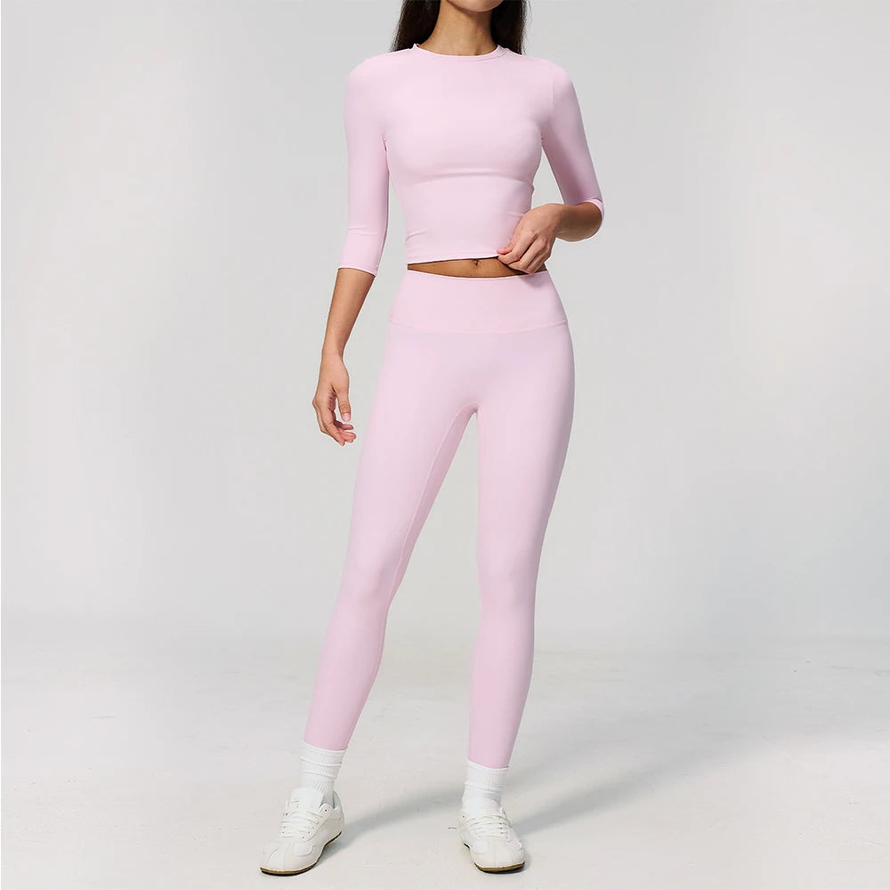 A woman wearing a light pink yoga and fitness leggings set consisting of a long-sleeved top and matching pants.