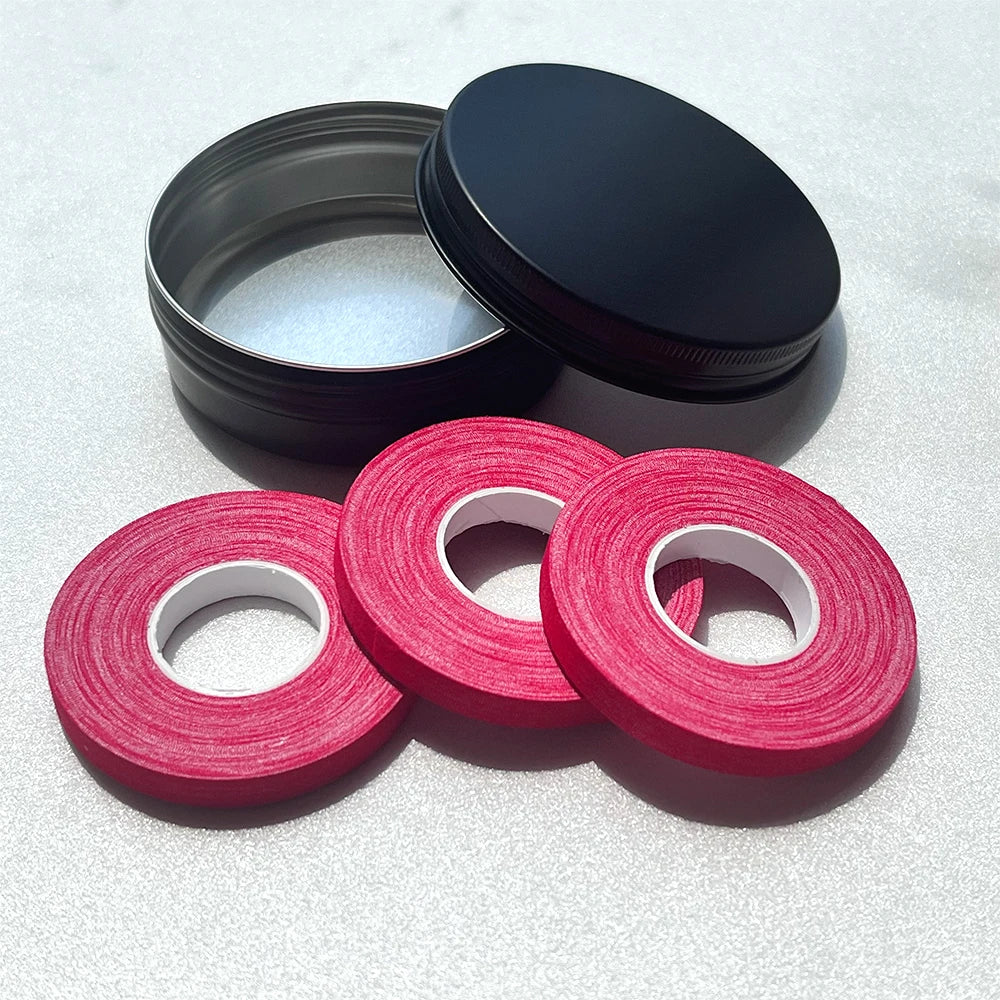 Rouleaux de ruban élastique rose vif et un couvercle noir sur une surface claire.