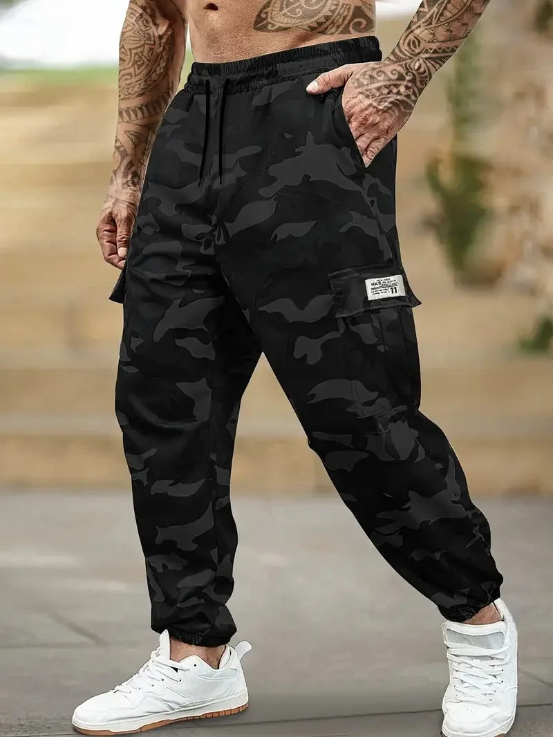 Un homme portant un pantalon cargo camouflage noir et des baskets blanches, montrant la coupe du pantalon.