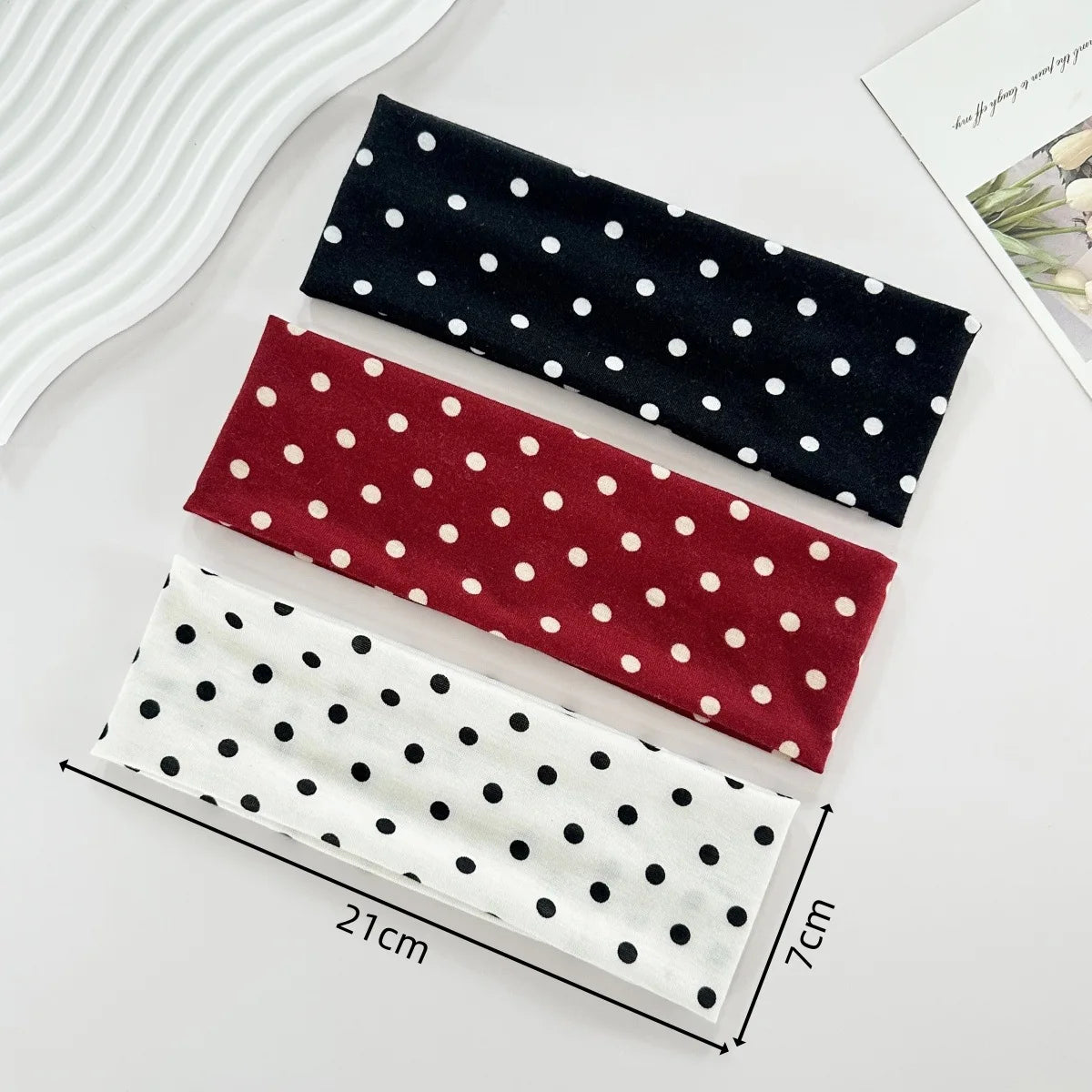 Trois bandeaux de yoga élastiques à pois noirs, marron et blanc présentés sur une surface blanche.