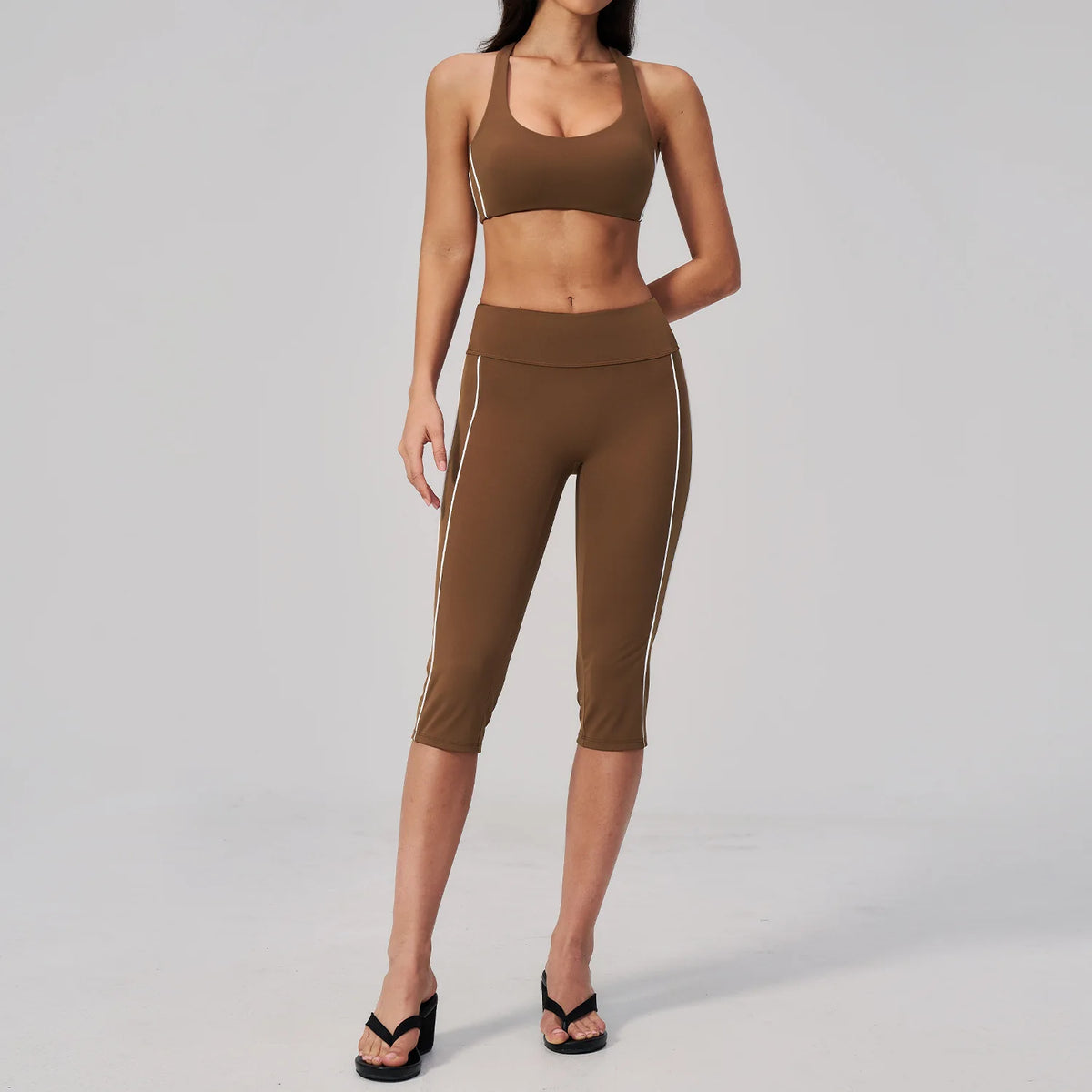A woman wearing a brown two-piece yoga and sports tracksuit set consisting of a cropped top and full-length leggings.