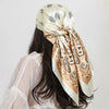 A woman is shown from the back wearing a beige silk paisley shawl scarf tied around her hair.