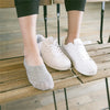 A pair of white boat shoes and a gray sock are resting on a wooden bench.