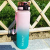A tall, translucent pink and blue sports water bottle with a black cap is placed outdoors on a stone surface.